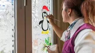 dorosla kobieta maluje pingwina farbami na szybie