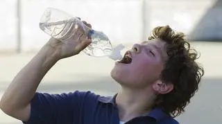 Spocony chłopiec pije wodę w upalny dzień