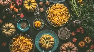 Makaron z dynią. Na stole leżą dynie jako ozdoba, a na talerzach nałożony jest makaron z dynią. 