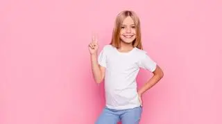 Dziewczynka w białej koszulce, dłonią pokazuje znak V