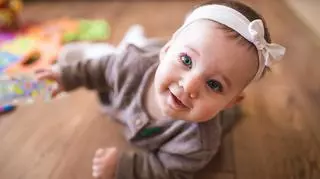 Zdjęcie dziecka podczas sesji zdjęciowej w domu. Dziewczynka z kokardą na głowie. 