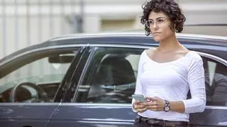 Kobieta w okularach stoi przy samochodzie