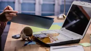 Przewracana filiżnaka i kawa wylewająca się na otwarty laptop