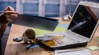 Przewracana filiżnaka i kawa wylewająca się na otwarty laptop