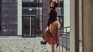Uśmiechnięta elegancka kobieta w spódnicy midi opiera się o balustradę. 