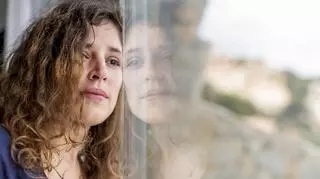 Smutna kobieta stoi przy oknie i patrzy w dal