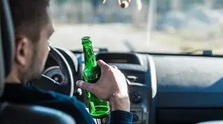Kierowca za kierownicą z piwem w ręku.