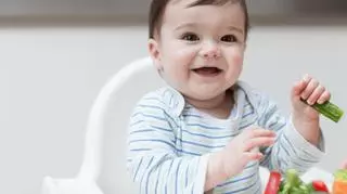 maly chlopiec niemowle w krzeselku do karmienia je warzywa usmiecha sie