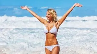 uśmiechnięta kobieta w białym bikini, rozkładająca dłonie w radosnym geście