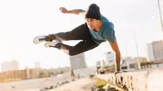 Młody mężczyzna uprawiający freerun, wykonujący akrobację na murze