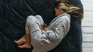 Kobieta w szlafroku na łóżku trzyma się za brzuch
