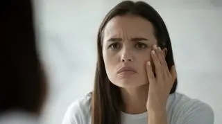 Kobieta przeglądająca się w lustrze, dotykająca dłonią twarzy