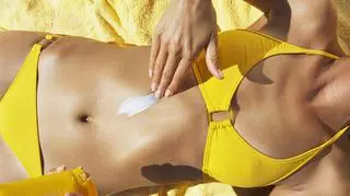 Kobieta w żółtym bikini kremuje skórę.