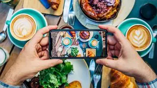 Stół zastawiony jedzeniem w obiektywie smartfonu. Trendy kulinarne.