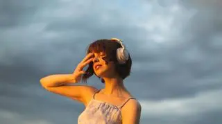 Kobieta słucha muzyki, w tle pochmurne niebo