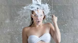 Kobieta biorąca prysznic w białym stroju kąpielowym.
