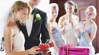 Młoda para otwierająca prezenty, w tle goście weselni.