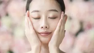Młoda kobieta z zamkniętymi oczami trzymająca dłonie na twarzy. Pielęgnacja skóry. Trendy urodowe.