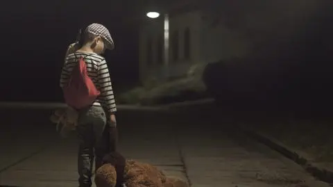 Pięciolatek wieczorem na podwórku w koszulce z krótkim rękawem.