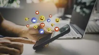 Fruwające emoji nad ekranem trzymanego w dłoniach telefonu