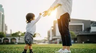 Dziecko stoi na trawie obok osoby dorosłej