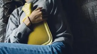Osoba z miesiączką, trzymająca termofor na brzuchu, skulona 