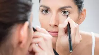Kobieta stojąca przed lustrem z eyelinerem w dłoni.