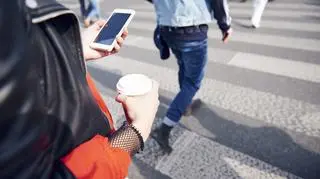 kobieta patrzy w telefon na przejściu dla pieszych