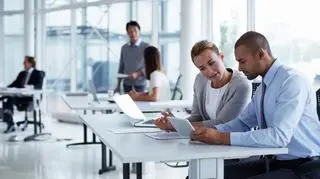 Mężczyzna i kobieta pochylają się nad tabletem w przestrzeni biurowej. 