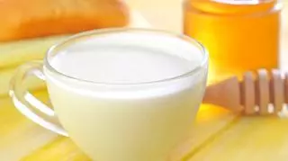 Mleko w filiżance stojące na stole obok słoika z miodem