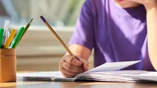 Dziecko pochylające się nad zeszytem z ołówkiem w dłoni. 