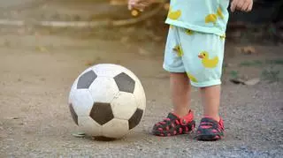 Dziecko stojące obok piłki do footbolu. 