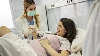 Pielęgniarka trzymająca za rękę ciężarną kobietę na sali porodowej.