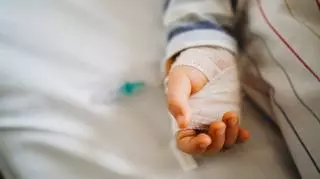 Zabandażowana dziecięca rączka na szpitalnym łóżku.