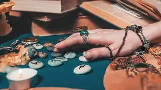 Kobieca dłoń w biżuterii nad kamieniami z runami