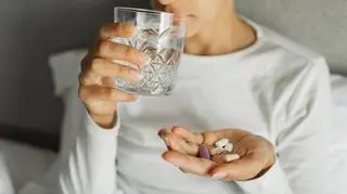 Osoba trzymająca w dłoni leki i szklankę wody