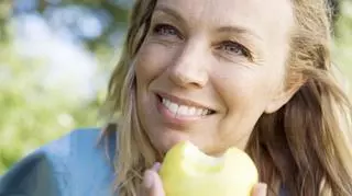 Kobieta w średnim wieku z nagryzionym jabłkiem w dłoni. 