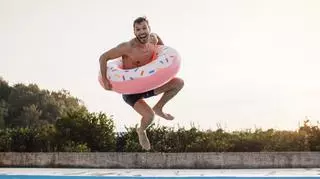 Mężczyzna skaczący do basenu z dmuchanym kołem do pływania.