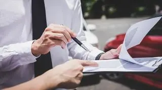 Osoby podpisujące dokumenty na tle samochodów