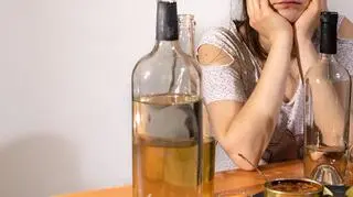 Osoba siedząca nad butelkami alkoholu