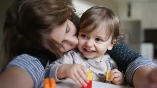 Mama przytula i całuje dziecko, które bawi się klockami