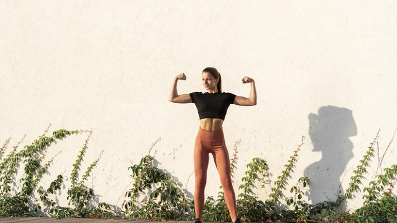 młoda kobieta w stroju sportowym pręży bicepsy, jak ćwiczyć bicepsy w domu