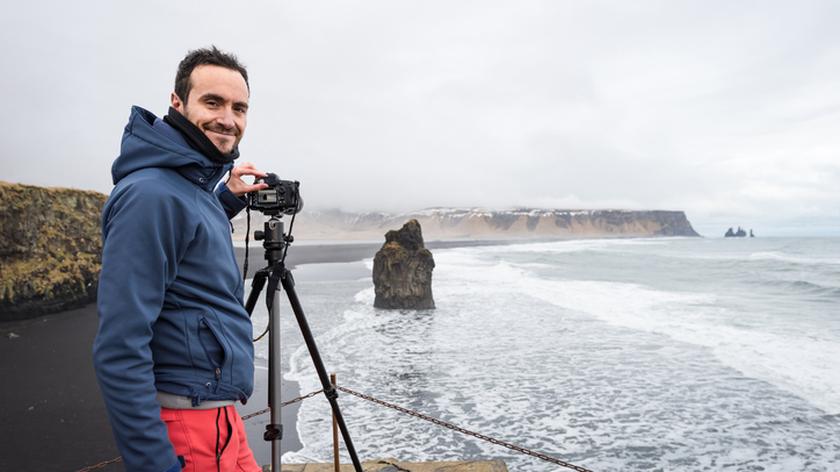 Mężczyzna stoi przy statywie z aparatem nad morzem