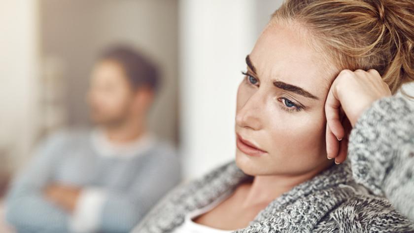 Smutna kobieta, w tle siedzi mężczyzna