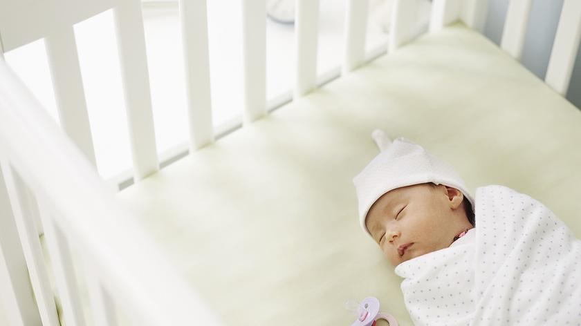 Łóżeczko dla dziecka. Małe dziecko leży i śpi w łóżeczku. 