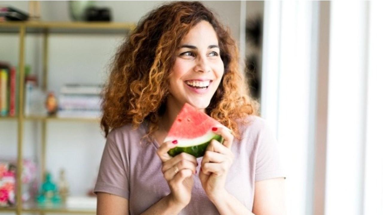 Uśmiechnięta kobieta trzymająca w dłoniach owoc arbuza