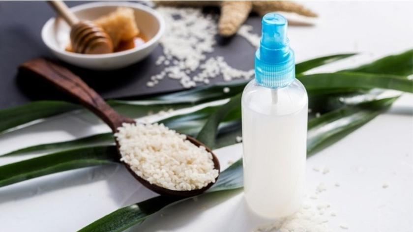 Butelka z atomizerem wypełniona białym płynem, obok drewniana łyżka z ryżem