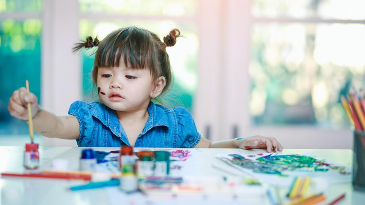 Dziewczynka siedzi przy biurku i maluje farbami