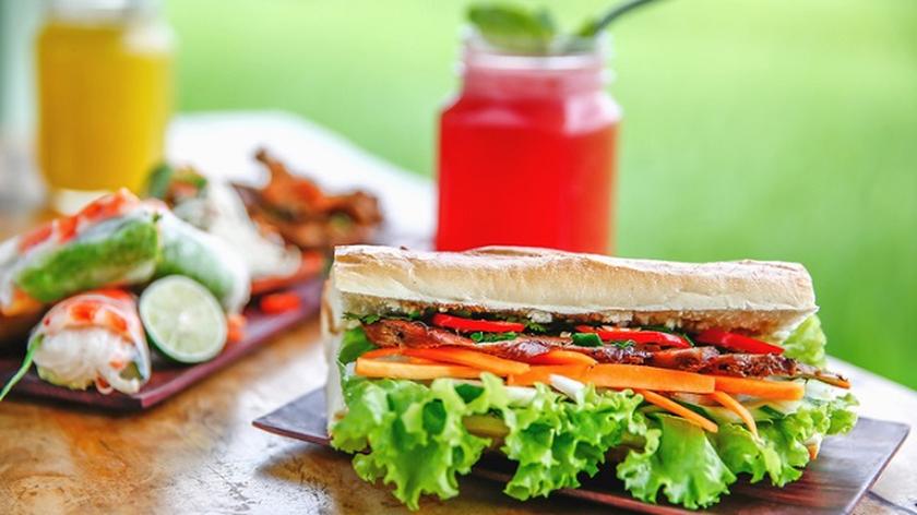 Banh mi, bagietka z warzywami i mięsem, w tle czerwony i pomarańczowy sok