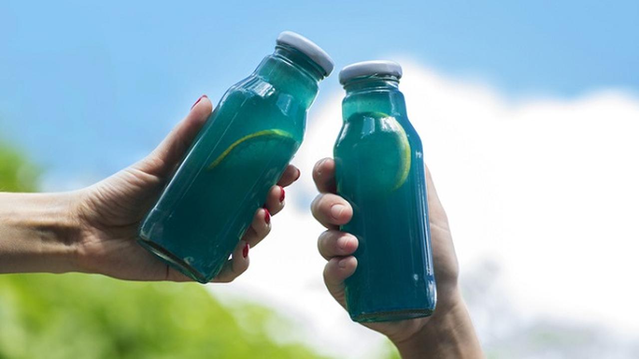 domowe isotoniki w niebieskich butelkach trzymane w dłoniach